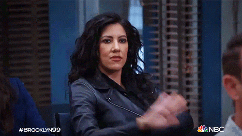 TV gif. Melissa Fumero as Amy from Brooklyn Nine-Nine high-fives Stephanie Beatriz as Rosa Diaz, both seated in the precinct.