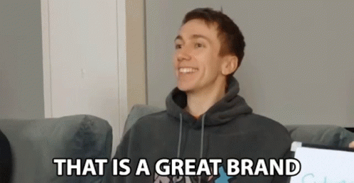 a young man in a hoodie is sitting on a couch and smiling .