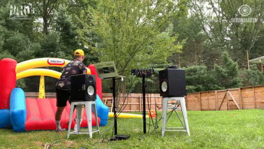 GIF of a man DJing in a backyard, and throwing a child into an inflatable bounce house