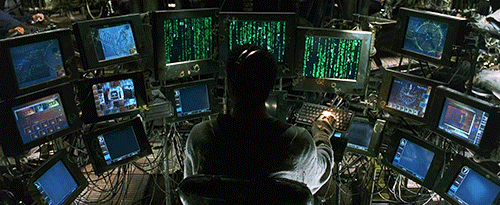 GIF of man sitting in front of many computer screens while working on code
