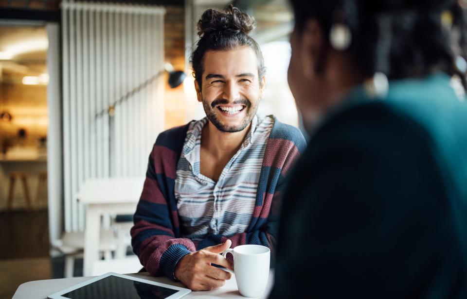 Man with coffee cup sitting at a table smiling