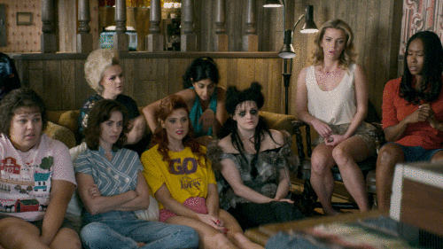 GIF of a group of women sitting on the floor keeping one of the women from standing up