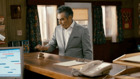 GIF of man in suit standing at a front desk pounding the bell with his fist