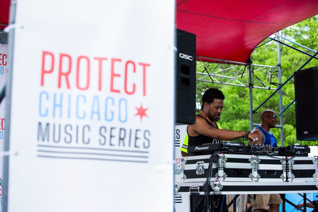 Male DJ performing with "Protect Chicago Music Series" sign in front of him