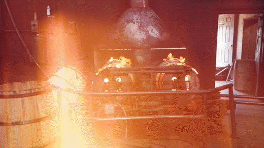 Log Still Distillery GIF with people cheering glasses, a water tower, and a roaring fire