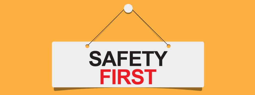 solid yellow background with white hanging sign displaying the words "Safety First"