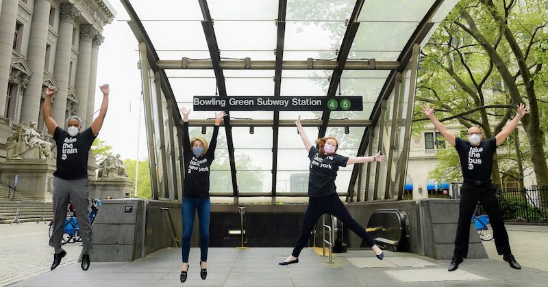 4 people jumping in the air in front of Bowling Green Subway Station in New York City.